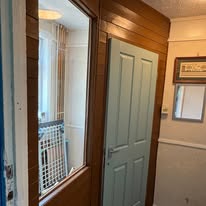 Light green four-panel door fitted next to a wood-panelled wall and mirrored cabinet