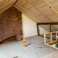 Freshly boarded loft room with exposed brick fireplace and new timber framing