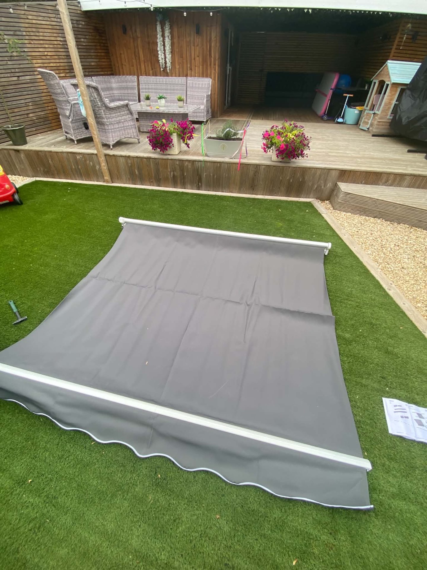 Grey outdoor awning unpacked and laid out on a lawn before installation