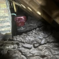 Loft insulation packed between timber joists next to a brick chimney breast