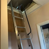 Silver loft ladder installed in a room with a tidy picture-frame surround