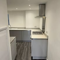 Compact grey kitchen fitted with white worktops and finished flooring