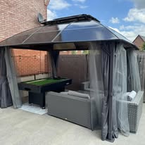 Gazebo with grey curtains, outdoor seating and a pool table installed on a patio