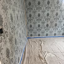 Grey damask wallpaper being prepared in a bedroom with dust sheets down
