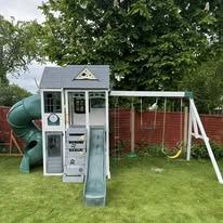Wooden playhouse with slide and swing set assembled in a garden